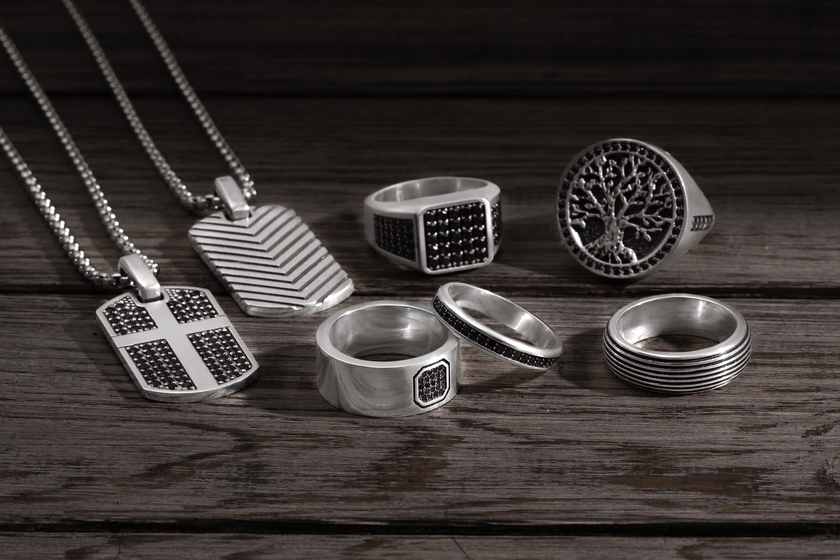 STRONZEN jewelry assortment with men's signet rings, pendants, and wedding bands on a wooden table.