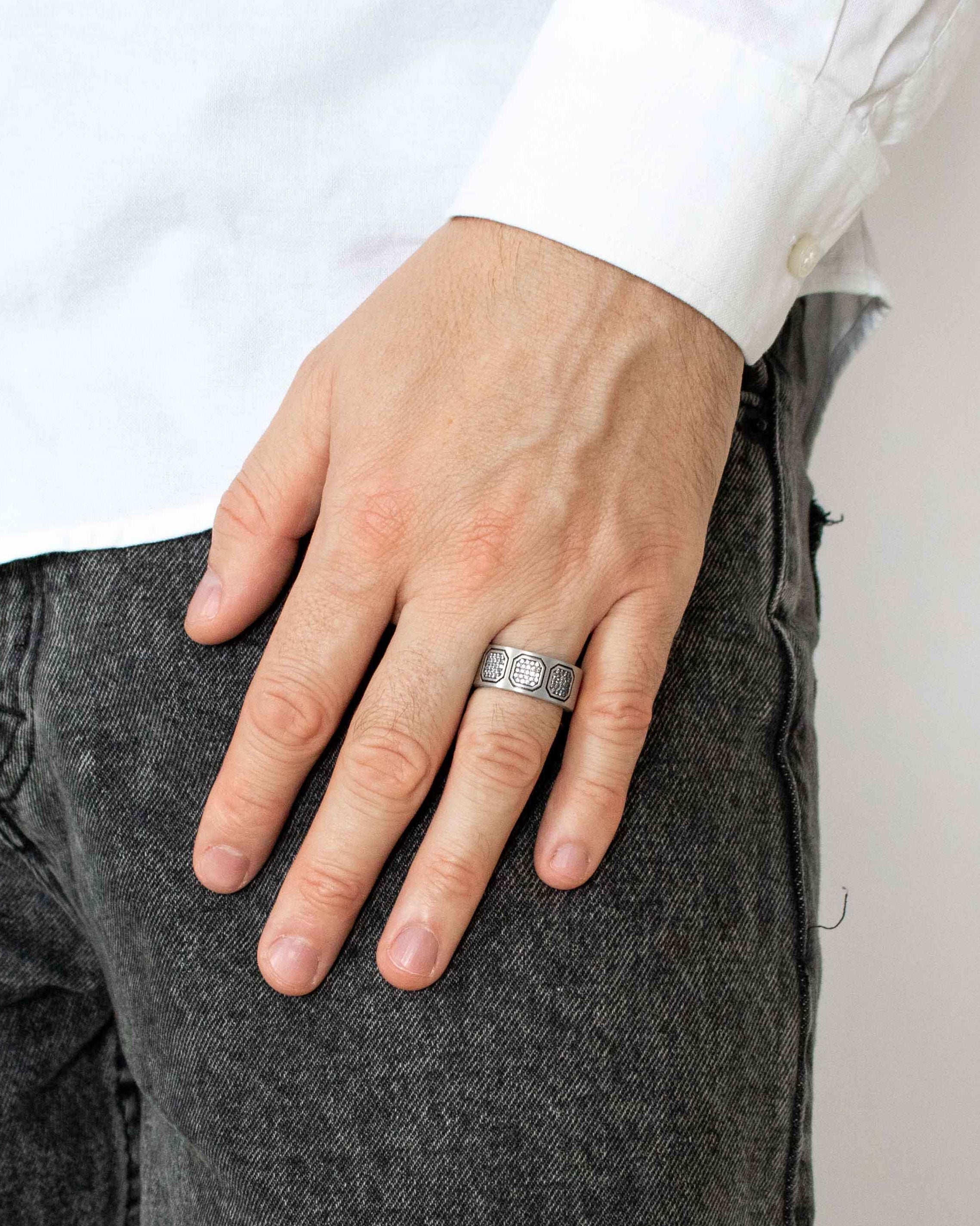 Hand wearing a ring with a white shirt and gray pants against a neutral background
