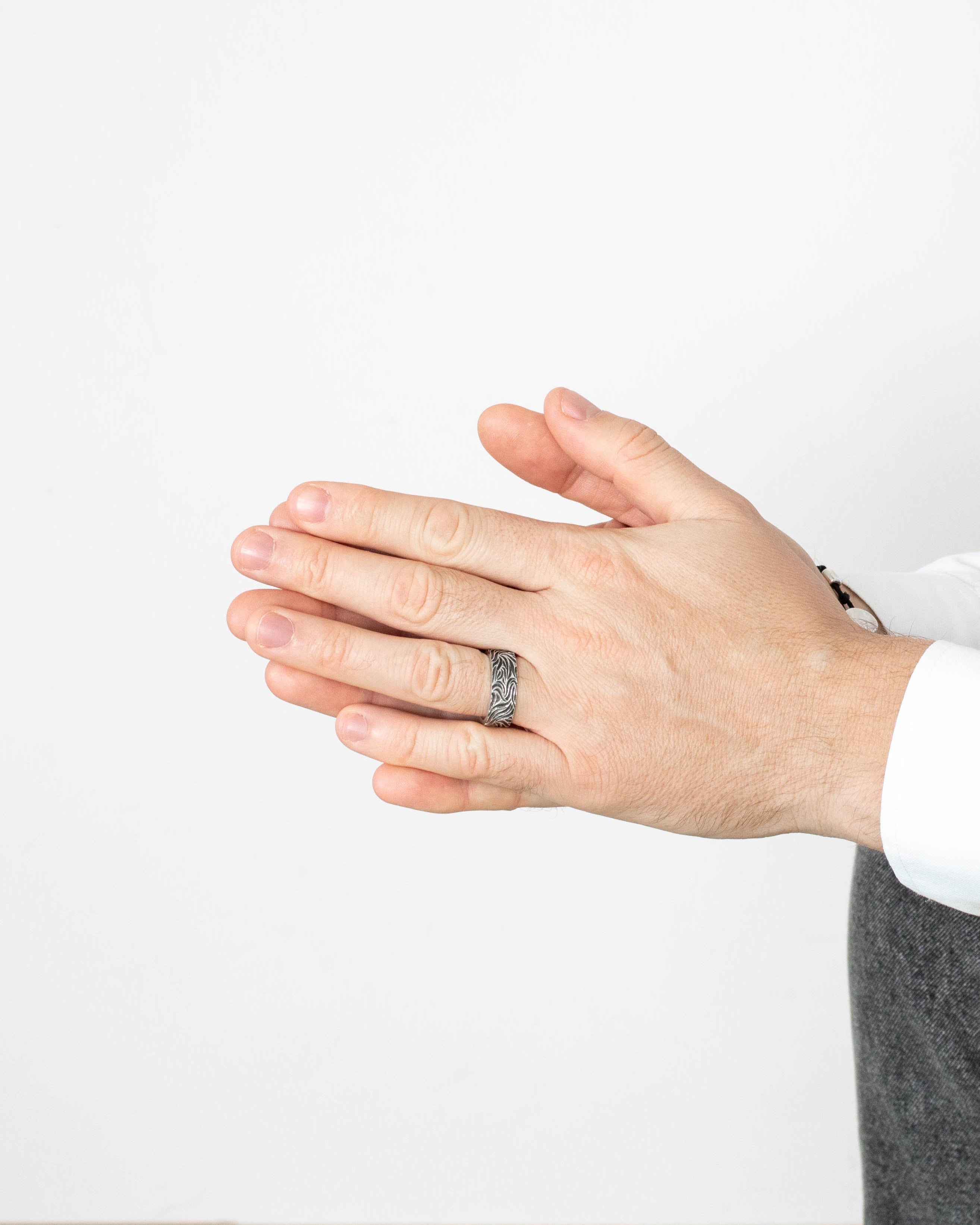 Hand wearing a silver ring on a plain background