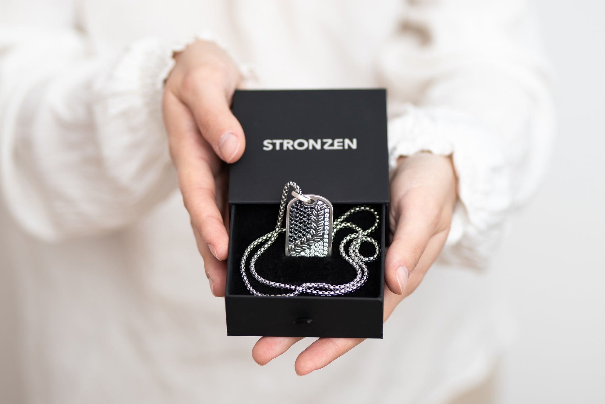 A woman shows a Stronzen gift box with a pendant necklace as a symbolic gesture of a perfect gift for men