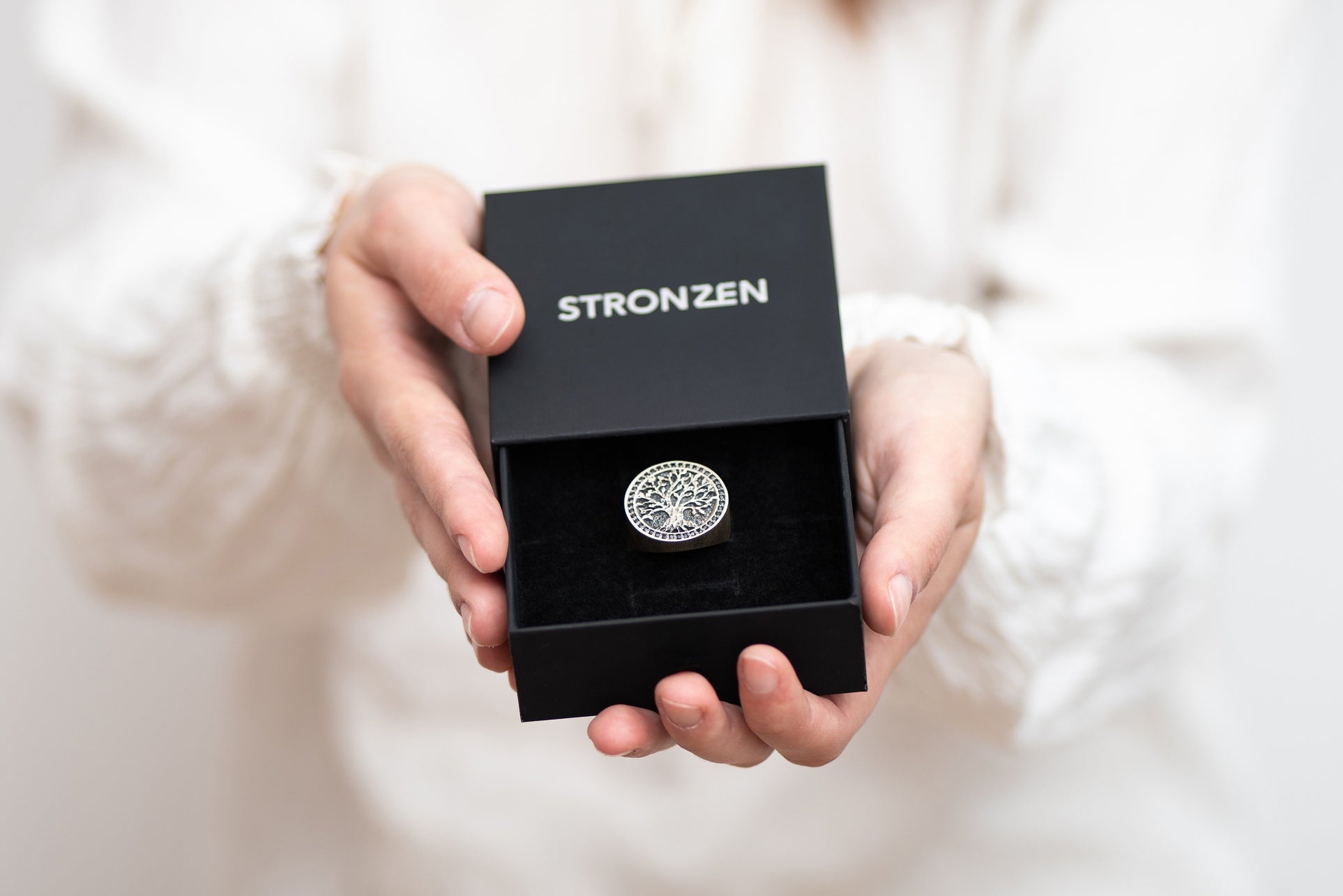 A woman presenting a Stronzen gift box with a signet ring as a symbolic gesture of a perfect men's jewelry gift.