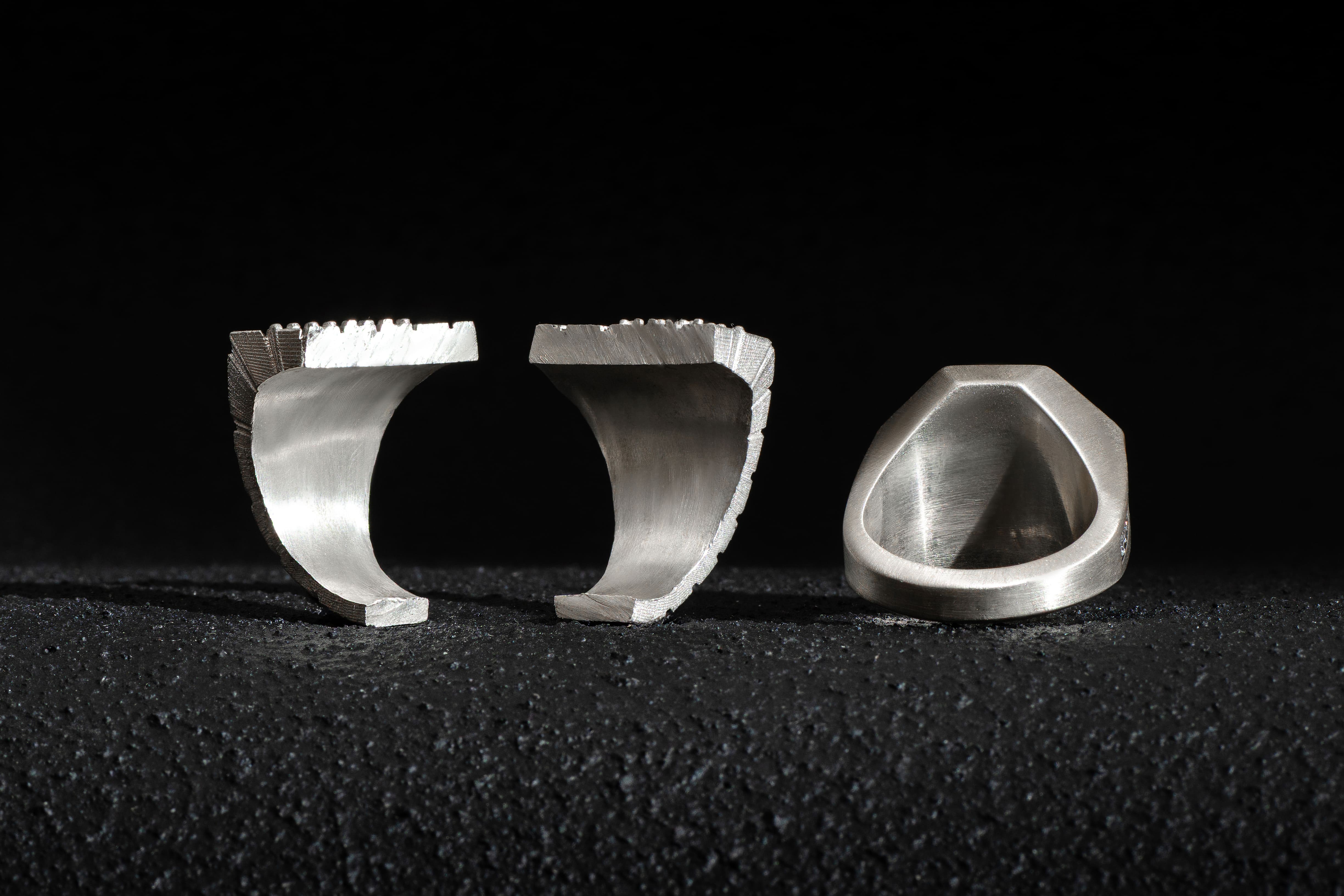 Two silver signet rings by Stronzen lying side by side. The ring on the left is cut in half to show its solid back and substantial weight.